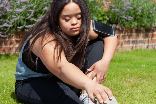 Young biracial woman with Down Syndrome in active wear and wearable tech stretching her legs