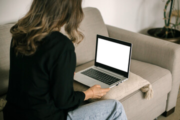 White screen on laptop. Mock up. Young woman working remotely on laptop computer at cozy home on...