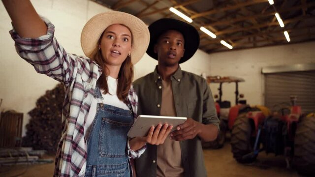 Caucasian female farmer holding digital tablet while mixed race male points around shed room