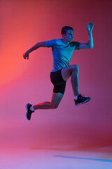 Fototapeta na wymiar Portrat of Caucasian professional male athlete, runner training isolated on pink studio background with blue neon filter, light. Muscular, sportive man.