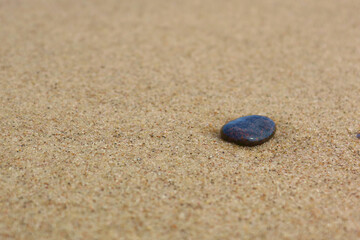 Fototapeta na wymiar Small stone on the sandy beach, closeup, selective focus