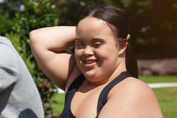 Naklejka na ściany i meble Portrait of young biracial woman with Down Syndrome in active wear tying her hair and smiling
