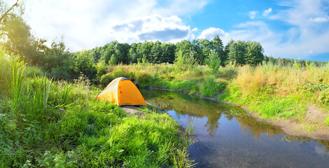 Orange tent on banks of small river with green banks