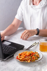 Noodles in a plate next to a girl at a laptop