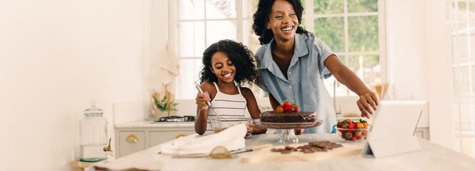 Mother and daughter having fun making cake with digital tablet