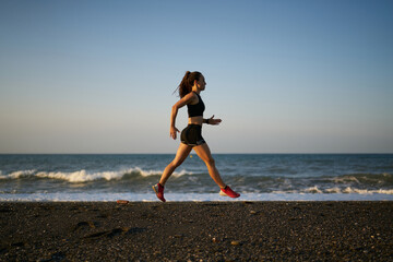 young professional female athlete running on a sunrise in the beach