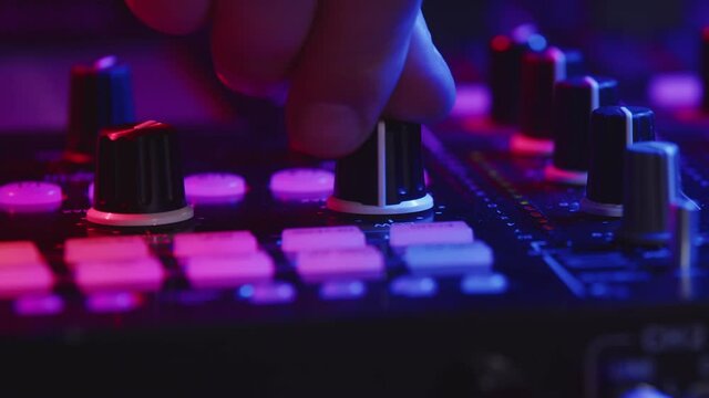 Professional DJ is adjusting fader on digital music console in pink neon light in nightclub. Male hand controls digital DJ console, closeup. Concept of party.