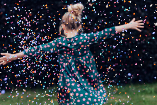 back view of beautiful little girl under a shower of confetti - birthday party carefree celebration concept