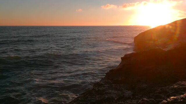 El mar y las olas rompiendo en las rocas, salpicando entre luz de sol de atardecer