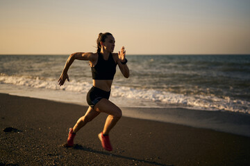 young professional female athlete running on a sunrise in the beach