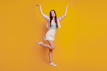Fototapeta na wymiar Photo of cheerful girl hold weighing hands up empty space isolated over yellow background