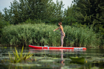 Fototapeta na wymiar Young Caucasian woman, sportsman, tourist standing on paddle board, SUP, practicing alone. Active life, sport, leisure activity concept