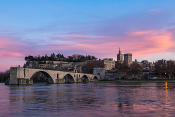 Fototapeta premium フランス 夕焼けに染まった空の下のアヴィニョンのサン・ベネゼ橋と後ろに見える城壁とノートルダム・デ・ドン大聖堂