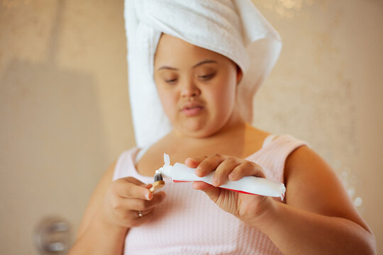 Young biracial woman with Down Syndrome applying toothpaste on bamboo toothbrush