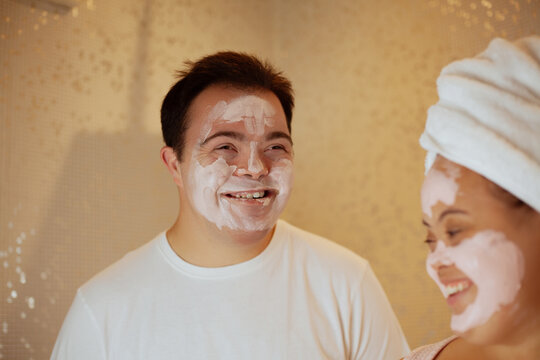 Young biracial couple with Down Syndrome with face masks having fun in the bathroom