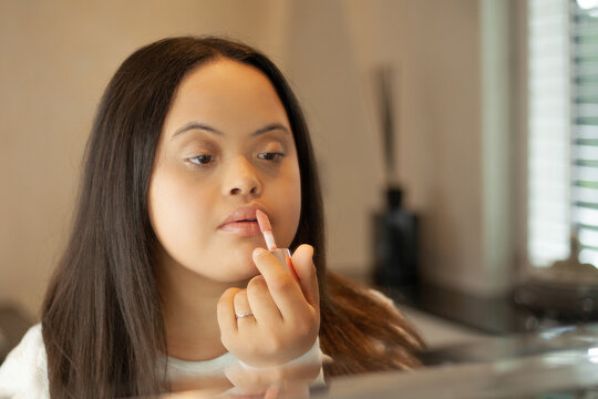 Young biracial woman with Down Syndrome applying lipgloss in the bathroom