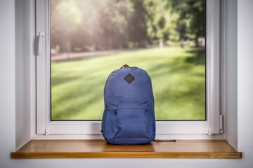 A school backpack on a wooden windowsill and an autumn landscape in the window with sunbeams 