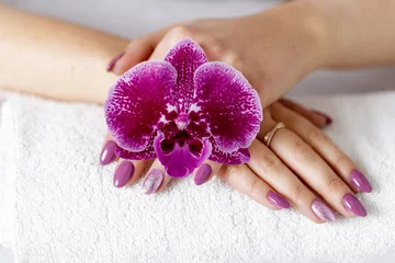 Poster Im Rahmen Beautiful hands with fresh manicure lying on a white towel and over lilac purple orchid flower. © BarTa