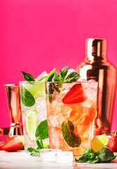 Couple of Mojito cocktails or mocktails with lime, rum, mint, strawberry and ice in glass on pink background