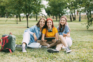Fototapeta premium Teenage girls sit on the green lawn in the park during a break. Education and knowledge, lifestyle of teenagers