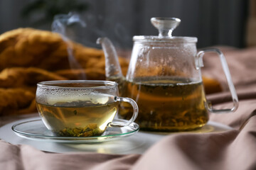 Tray with cup of hot tea and teapot on bed