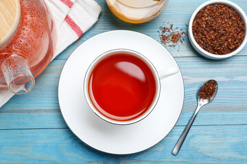 Freshly brewed rooibos tea and dry leaves on light blue wooden table, flat lay
