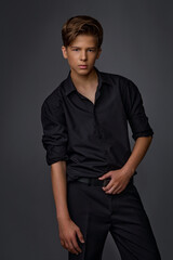 guy teenager in a black shirt and black trousers posing in the studio on a gray background 