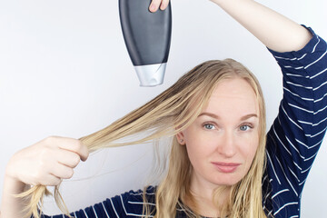 Fototapeta premium The girl looks in the mirror at her oily hair, then takes a shampoo to treat oily hair. Problematic scalp and increased secretion of the sebaceous glands. Cosmetology diseases treatment concept
