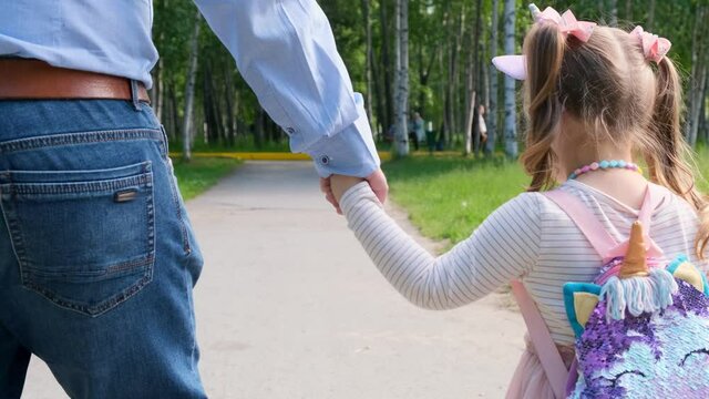 Cheerful Dad and daughter 3-4 years old go and hold hands on a walk in the park. Dad day. Happy childhood concept. back view