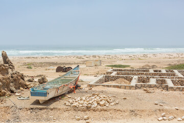 small fishery boat and remaining foundation of the stone house beside the beach of arabian sea in...
