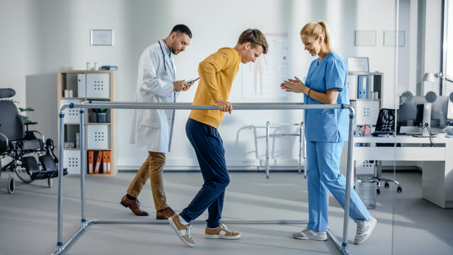 Hospital Physical Therapy: Strong Patient with Injury Making First Steps, Walks Holding for Parallel Bars. Physiotherapist, Rehabilitation Doctor Assist, Help Disabled Person.
