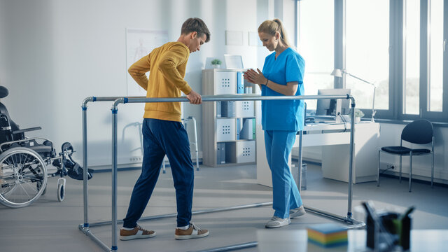 Hospital Physical Therapy Room: Strong Patient with Injury Walking Holding for Parallel Bars, Physiotherapist Encourages Assists, Helps Disabled Person Do Rehabilitative Physiotherapy.