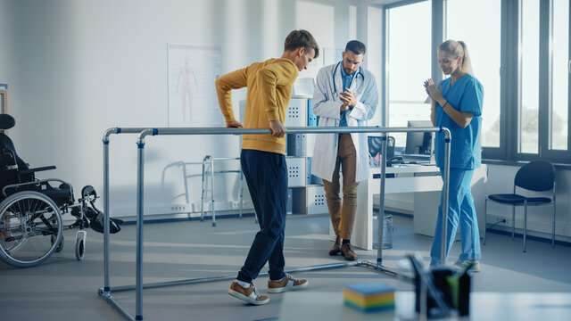 Hospital Physical Therapy: Strong Patient with Injury Making First Steps, Walks Holding for Parallel Bars. Physiotherapist, Rehabilitation Doctor Assist, Help Disabled Person.