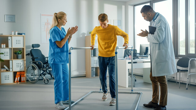 Hospital Physical Therapy: Portrait of Strong Young Male Patient with Injury Successfully Walks Holding Parallel Bars. Physiotherapist, Rehabilitation Doctor, Help, Assist, Disabled Person