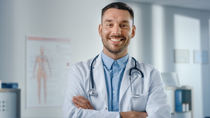 Portrait of Handsome Caucasian Medical Doctor Wearing White Coat and Stethoscope Crosses Arms, Standing in His Health Clinic Office. Successful, Confident Physician Looks at the Camera, Smiles