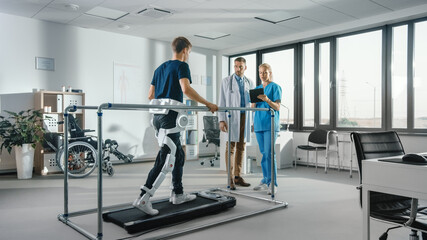 Modern Hospital Physical Therapy: Patient with Injury Walks on Treadmill Wearing Advanced Robotic Exoskeleton. Physiotherapy Rehabilitation Scientists, Engineers, Doctors use Tablet Computer to Help - obrazy, fototapety, plakaty
