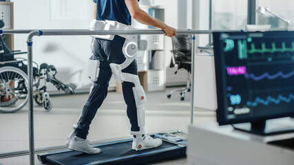 Modern Hospital Physical Therapy: Patient with Injury Walks on Treadmill Wearing Advanced Robotic...