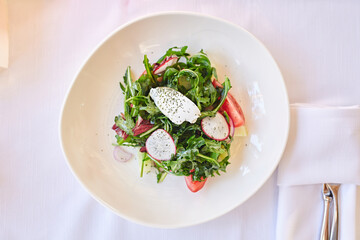 Green vegan salad from green leaves mix, vegetables and goat cheese. Top view on table. Selective focus