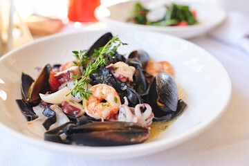 Delicious cuttlefish ink pasta with seafood. Black spaghetti made of squid ink with shrimps and other seafood. Black spaghetti pasta with seafood mussels in shells shrimp. Selective focus 