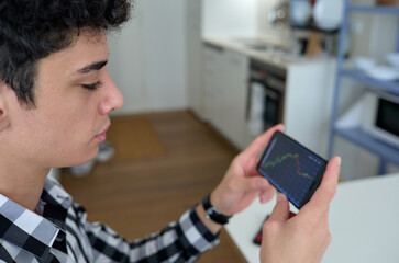 portrait of young man looking at a mobile in the home kitchen