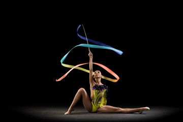 One sportive emotional girl, rhythmic gymnastics artist isolated on dark background in ray of...