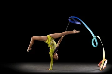 Foto op Plexiglas Slim sportive girl, rhythmic gymnastics artist in bright stage costume isolated on dark studio background in ray of light. Concept of sport, action, aspiration, active lifestyle © master1305