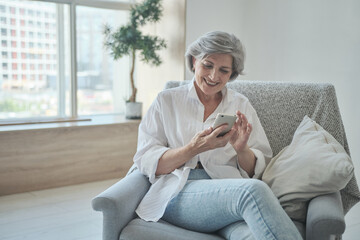 Relaxed mature elderly woman exploring mobile phone apps chatting on social media or purchasing online, smartphone scrolling social media swiping browsing, aged entrepreneur investment and trading.