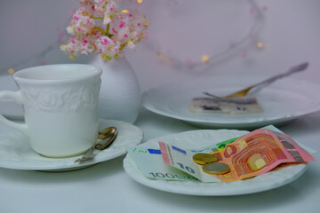 close-up of a white plate for money, euro banknotes and coins, Restaurant bill, cup of coffee, delicate pink flowers, dishes with food, the concept of tip money, change of the waiter