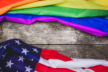 two flags on a wooden table, one flag is united states the second ist the rainbow flag