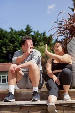 Young biracial couple with Down Syndrome in active wear sitting next to each other and high-fiving