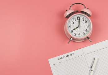 flat lay of habit tracker book, pink vintage alarm clock on pink background.