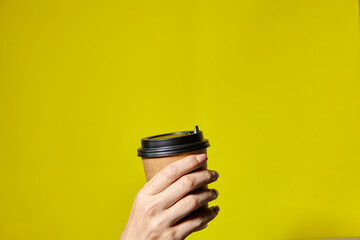 Hands holding two cups brown paper with black lid. Two coffee special offer or promo. Hands holding two cups on yellow screen background. Tea or Coffee to go. Brown paper cup with black lid.