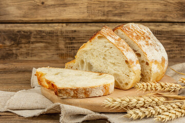 Freshly baked bread with wheat ears, fragrant pieces on a cutting board
