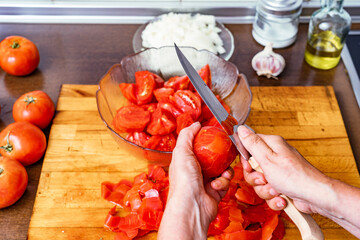 Persona pelando y cortando tomates rojos de la huerta para hacer tomate frito con ajo, cebolla, sal...